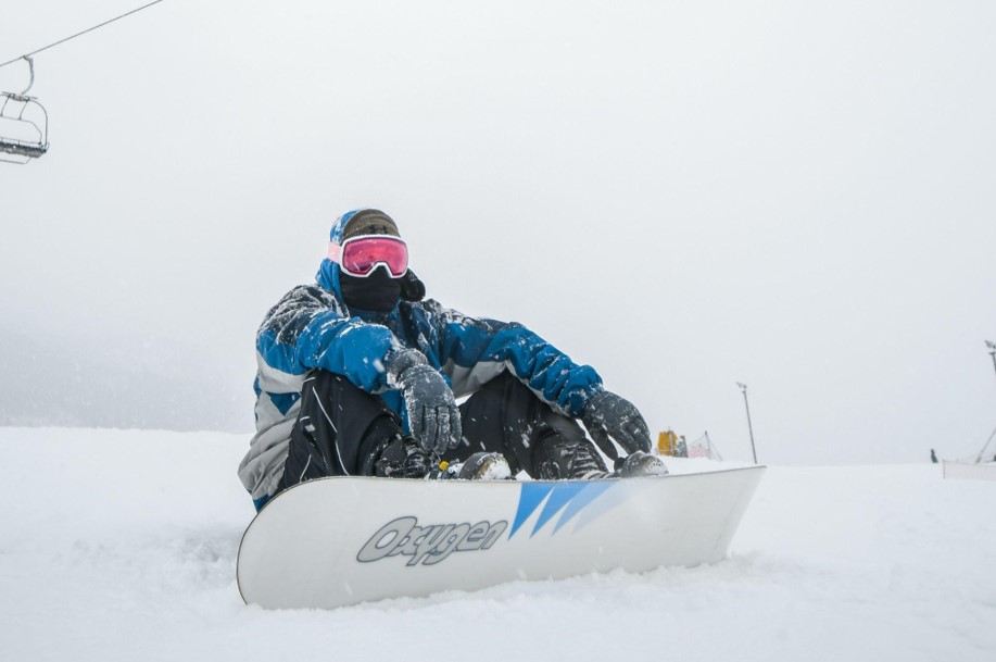 man sitting with a snowboard under cable cars